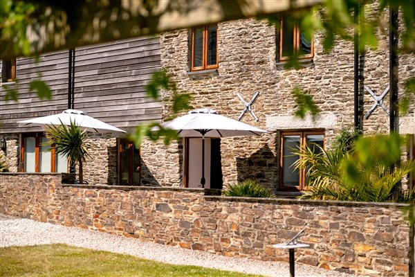 View of the extra of the Corn Barn with stone walls and garden seating and parasols at the front.